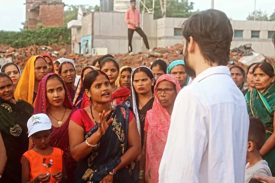 A man addresses a crowd of South Asian women and children outdoors near a construction site or rubble A man addresses a crowd of South Asian women and children outdoors near a construction site or rubble