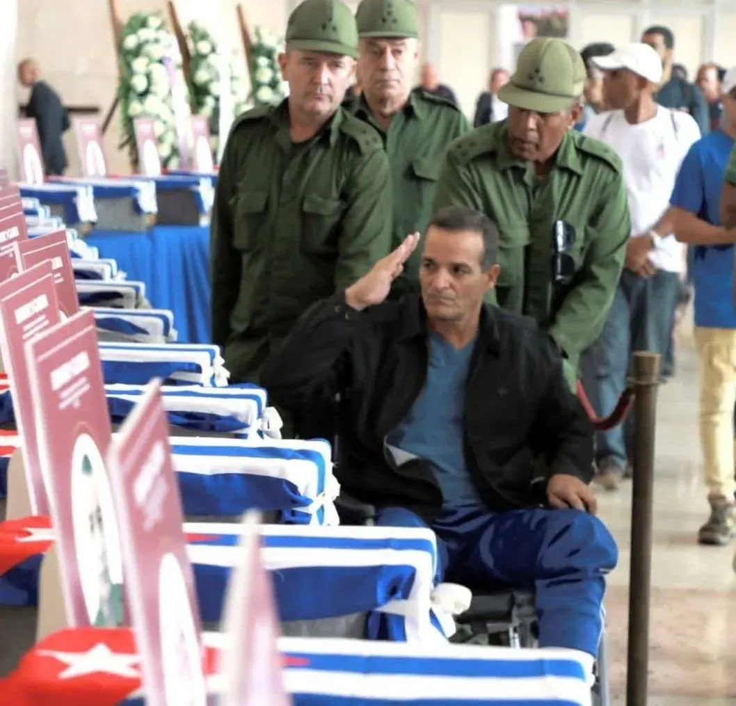 Funeral ceremony with coffins draped in Turkish flags, a man in a wheelchair saluting, and uniformed guards standing nearby